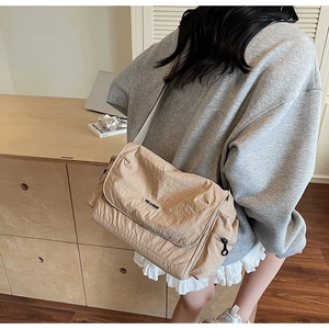 Detail of a large beige crossbody tote bag with wrinkled texture and adjustable strap