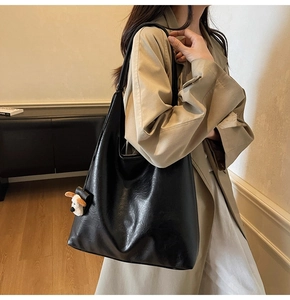 Close-up of black leather tote bag on model shoulder with cute dog plush charm pendant