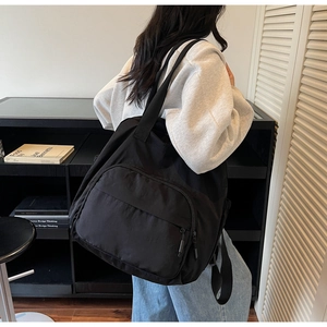 Detail view of large capacity black nylon tote bag worn over the shoulder in a lifestyle setting