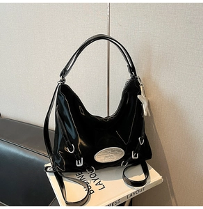 Detail of glossy black patent leather crescent bag with star pendant and silver plaque