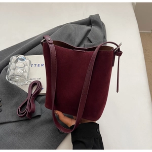 Macro detail of wine red suede bucket bag with leather trim and adjustable shoulder strap