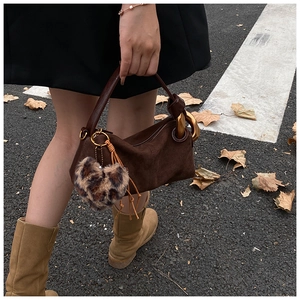 Detail of dark brown suede handbag featuring a gold metal ring handle and leopard heart charm
