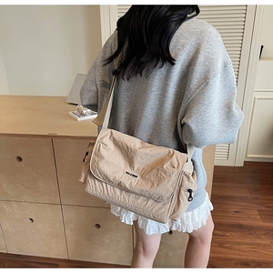 Detailed view of beige nylon messenger bag with wide strap in a minimalist cafe setting