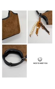 Détail d'un sac seau en daim marron avec surpiqûres losanges et breloque en perles