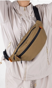 Detail der Nylon-Brusttasche mit Karomuster, Reißverschluss und orangefarbenem Etikett