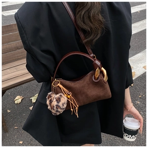 Detail of dark brown suede crossbody bag with gold hardware and leopard heart charm