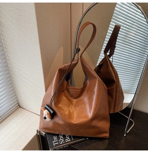 Brown leather tote bag with a cute plush puppy pendant placed on a black book