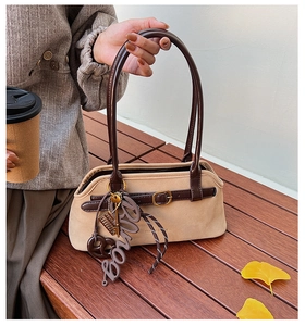 Detail view of beige suede tote bag featuring brown leather straps and vintage charms