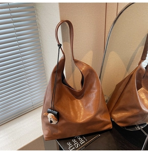 Detail view of brown matte leather tote bag featuring a cute cartoon dog plush charm