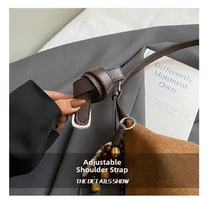 Detail of adjustable leather strap and beaded charm on a brown suede tote bag