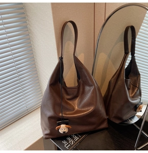 Detail of a brown leather tote bag with a cute plush dog pendant in a warm indoor setting