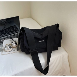 Detail view of a black nylon crossbody tote bag with wide strap and side zip pocket