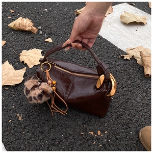 Detail of dark brown leather pillow bag with gold clasp and leopard print charm