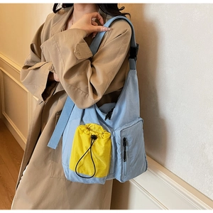 Dettaglio della borsa a tracolla in tela blu con tasche e tracolla larga indossata dal modello