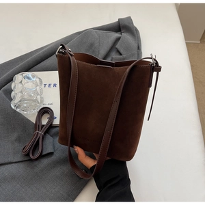 Detail of dark brown suede bucket bag with embossed logo on a minimalist background