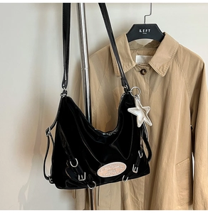 Detail of a black patent leather tote bag with silver hardware and star charm accessory