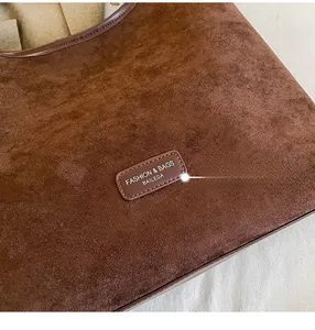 Close-up of dark brown suede mini bag with embossed leather logo and soft texture