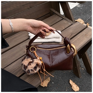 Detail of dark brown oil wax leather handbag with golden ring and leopard heart charm