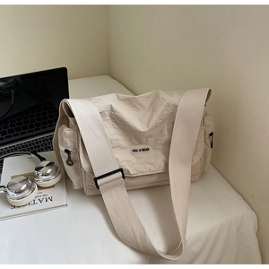 Detail view of cream nylon messenger bag with logo patch and adjustable wide strap