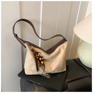 Close-up of beige suede tote bag with brown leather strap and wooden bead tassel details