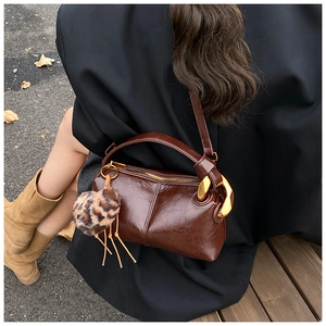 Dark brown leather pillow bag with gold buckle and leopard charm shown in outdoor autumn setting