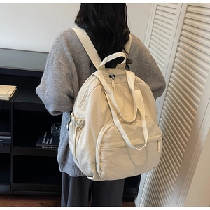 Model wearing a minimalist cream white multi-pocket backpack in a cozy home setting