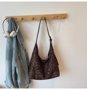 Leopard print hobo bag with long strap hanging on a wooden rack with a denim jacket