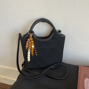 Détail du sac seau matelassé noir avec pendentif en perles de bois et poignée en cuir