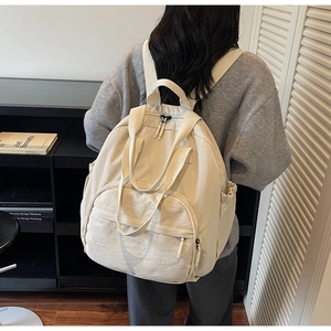 Rear view of model wearing a minimalist beige nylon backpack in a cozy home library setting