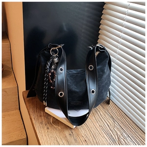 Detail of black textured leather crescent bag with silver eyelets and a decorative charm