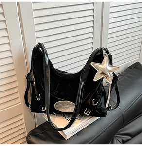 Detail of black patent leather hobo bag with silver rings and star-shaped pendant charm