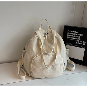 Close-up of the beige nylon backpack showing multi-pocket structure and handle details
