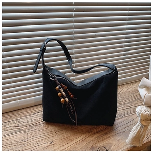 Detailed shot of a black crescent tote bag featuring a vintage wooden beaded tassel charm