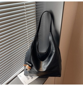Detail of black glossy crinkled leather tote bag with a cute plush dog charm pendant