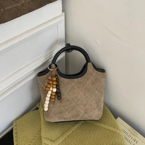 Détail du sac seau en suède avec motifs matelassés, glands en bois et poignées rondes