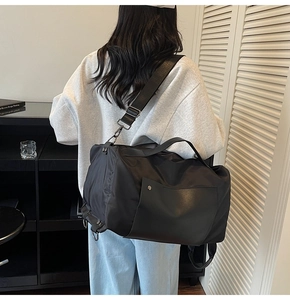 Rear view of a model carrying a large black waterproof nylon travel bag with shoulder straps