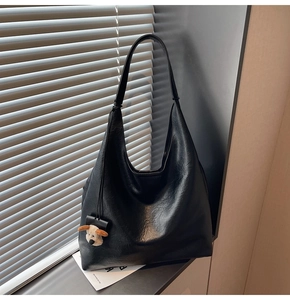 Detail of black faux leather hobo bag with plush puppy charm on minimalist background