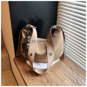 Detail of a khaki leather hobo bag featuring wide strap with silver eyelets and side tag