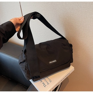 Detail of black canvas messenger bag featuring a wide strap and brand label on the front
