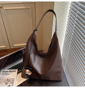 Detail shot of a brown leather tote bag with a cute sheep plush charm on a desk