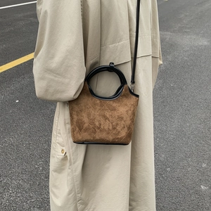 Détail d'un sac seau en daim marron avec surpiqûres matelassées et poignée ronde noire