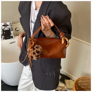 Close-up of brown leather Boston bag featuring golden buckle and leopard fur pompom