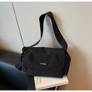 Detail of black nylon crossbody bag with flap closure and logo on a book base