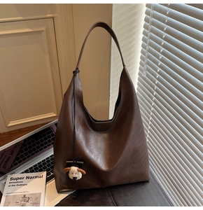 Detail of dark brown leather hobo bag with a cute sheep charm on a wooden desk