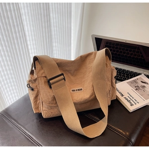 Detail view of khaki canvas crossbody bag with wide strap and brand label on desk