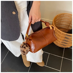 Close-up of vintage brown leather handbag featuring a leopard print pom-pom and gold hardware