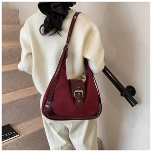 Burgundy hobo shoulder bag with matte fabric and shiny patent leather strap on a model