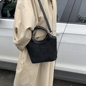 Gros plan du sac seau en daim noir avec motif matelassé et poignée ronde rigide