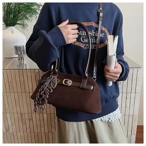 Detail of brown suede shoulder bag with buckle strap and knotted rope charm accessory