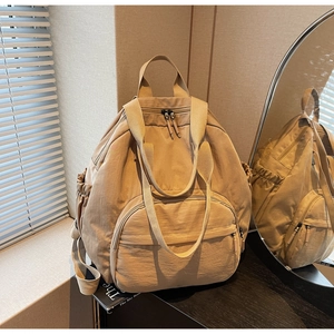 Detail of khaki nylon backpack featuring large front zipper pocket and drawstring sides
